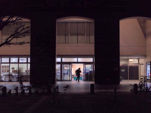 A photo at night time. There's a person stepping out of a grocery store. You can only make out the shadow of that person.